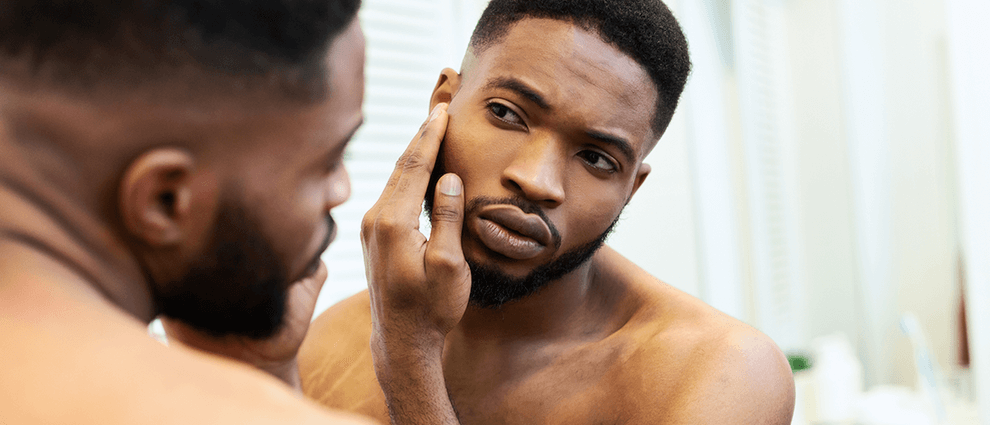 Barba crescer: homem negro e jovem confere a aparência de sua barba em frente ao espelho.