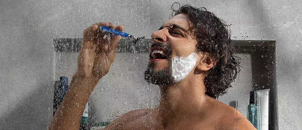 Barba no banho: homem branco jovem se divertindo durante o banho cantando com o aparelho de barbear em frente ao rosto.