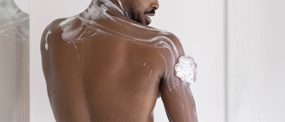 Sabonete: homem negro com barba ensaboa o corpo e o rosto durante o banho.