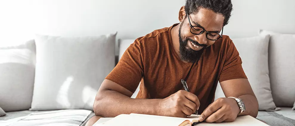Vida organizada: homem negro jovem sorri ao escrever em um caderno.